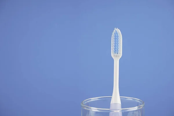 Een Tandenborstel Met Borstel Glazen Beker Tegen Blauwe Achtergrond — Stockfoto