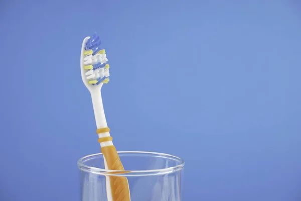 Een Tandenborstel Met Borstel Glazen Beker Tegen Blauwe Achtergrond — Stockfoto