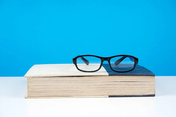 black frame eyeglasses on closed book against blue wall