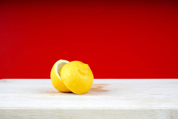 белый деревянный стол с нарезанными лимонными частями на фоне красной стены
  