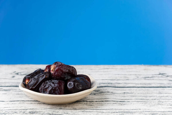 dry dark blue dates fruits in bowl plate, grey wooden table surface 