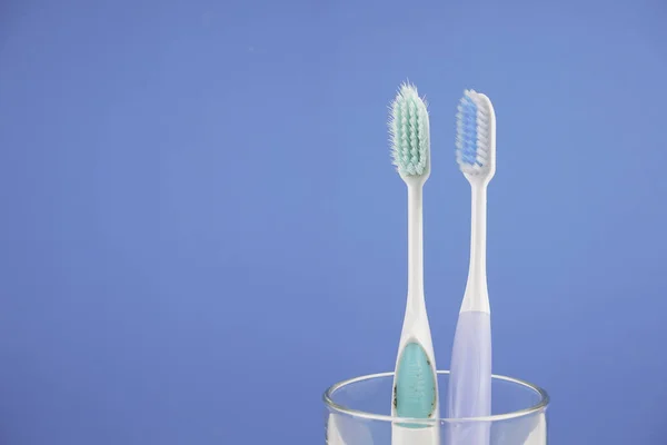 Duas Escovas Dentes Copo Vidro Contra Fundo Azul — Fotografia de Stock