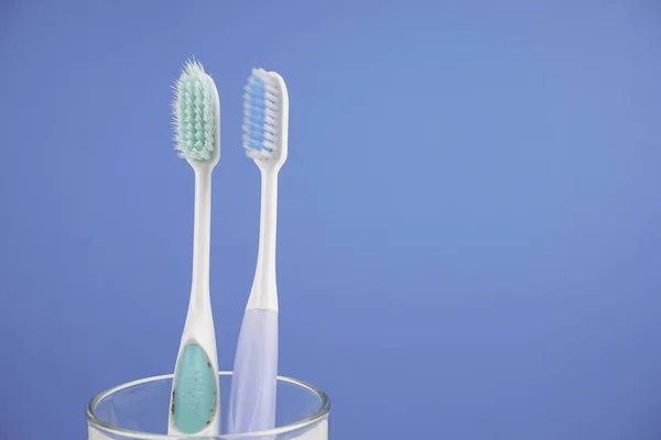 Duas Escovas Dentes Copo Vidro Contra Fundo Azul — Fotografia de Stock