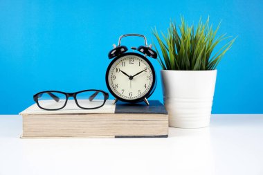 mavi duvara karşı kapalı kitap gözlük, pota bitki ile alarm vintage analog saat 