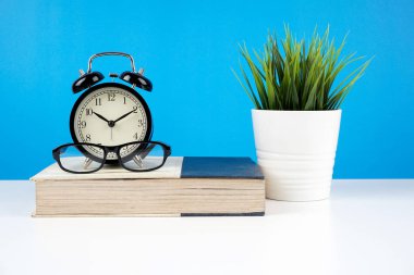 mavi duvara karşı kapalı kitap gözlük, pota bitki ile alarm vintage analog saat 