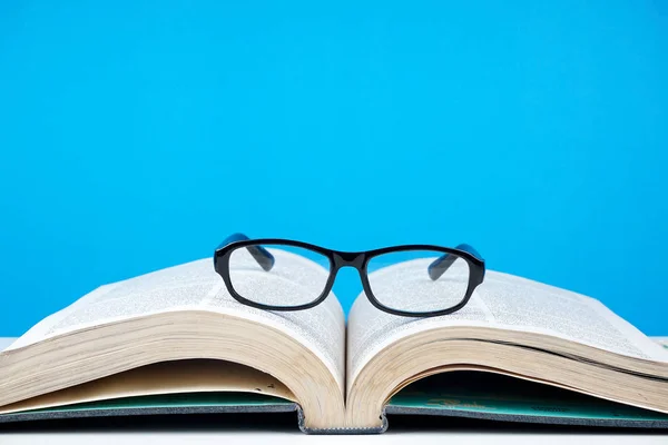black frame eyeglasses on opened book against blue wall