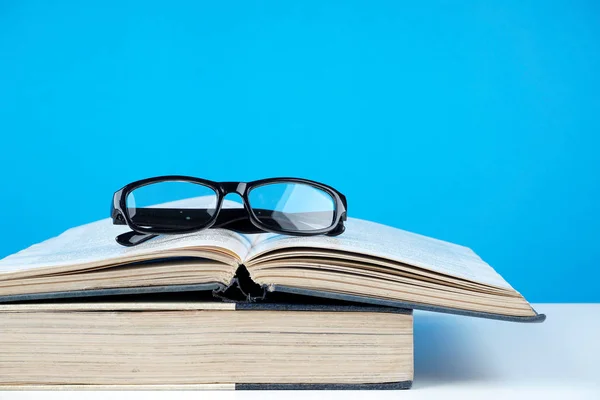 black frame eyeglasses on opened books against blue wall