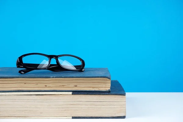 black frame eyeglasses on books against blue wall