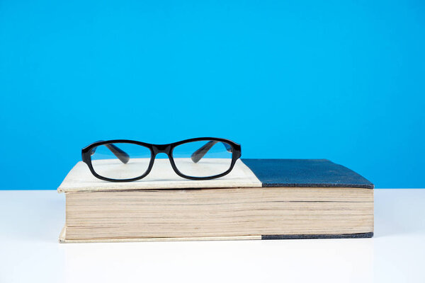 черные очки рамка на закрытой книге против синей стены
 