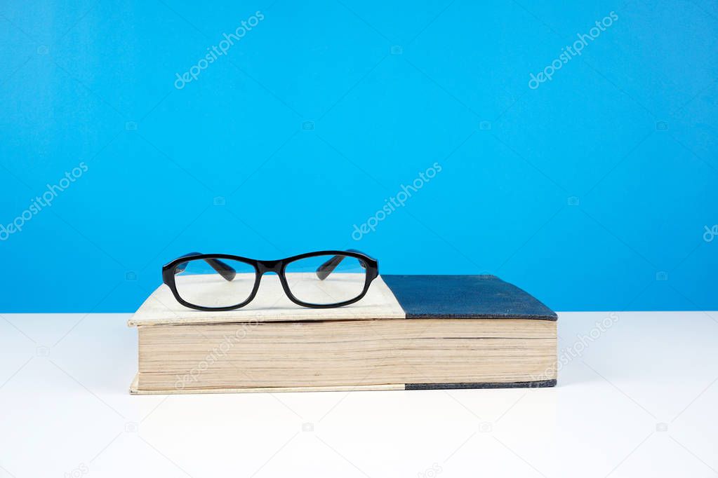 black frame eyeglasses on closed book against blue wall 