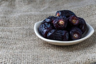 Koyu mavi hurma tabağındaki meyveler, çuval bezli masa. 