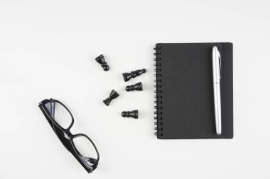 satranç taşları. beyaz yüzeyde gözlük, kağıt ders kitabı ve kalem  