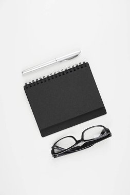 beyaz yüzeyde gözlük, kağıt ders kitabı ve kalem  