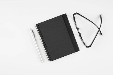 beyaz yüzeyde gözlük, kağıt ders kitabı ve kalem  