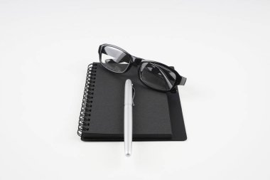 beyaz yüzeyde gözlük, kağıt ders kitabı ve kalem  