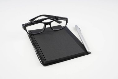 beyaz yüzeyde gözlük, kağıt ders kitabı ve kalem  