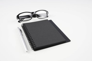 beyaz yüzeyde gözlük, kağıt ders kitabı ve kalem  