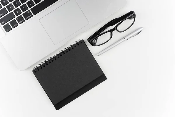workplace table with eyeglasses, paper textbook and pen on white surface with laptop