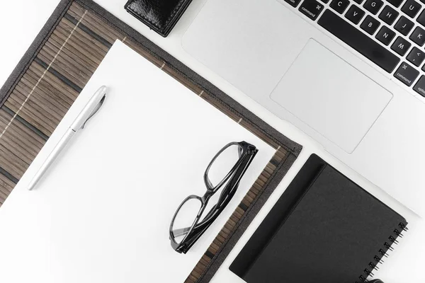 workplace table with eyeglasses, paper textbook and pen on white surface with laptop