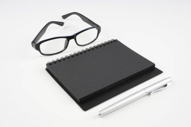 beyaz yüzeyde gözlük, kağıt ders kitabı ve kalem  