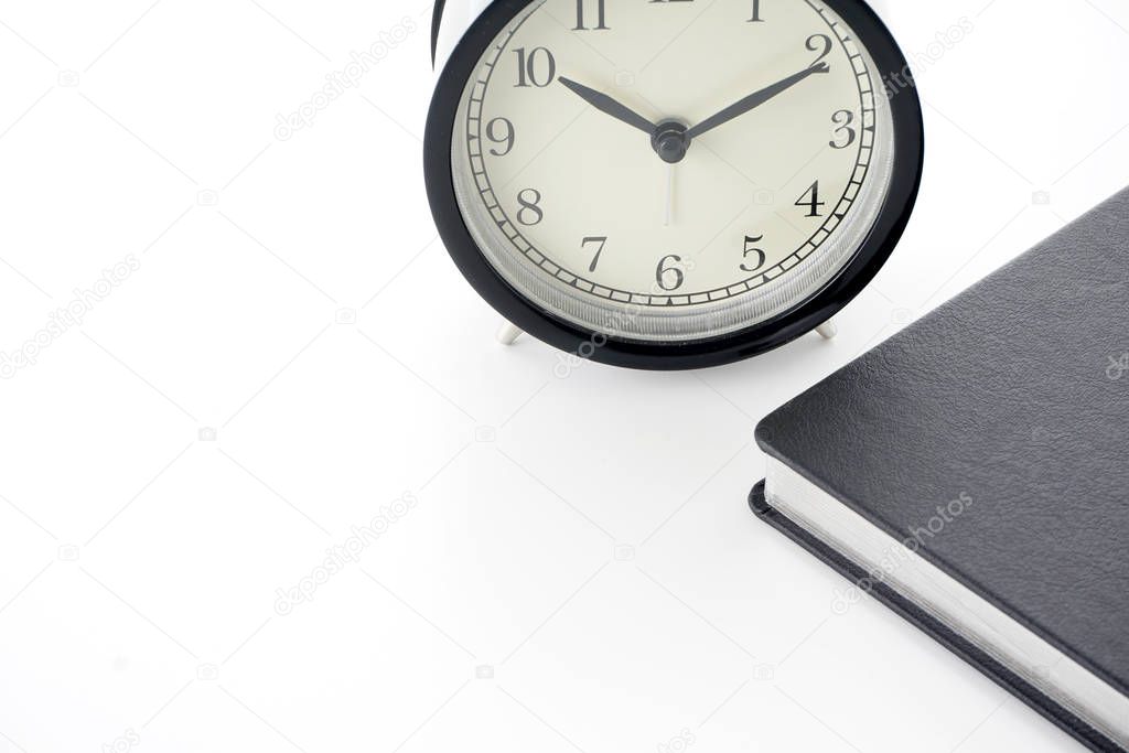 partial view of black cover paper textbook diary and vintage old analog alarm clock 