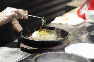 Şef mutfakta cızırdayan tabakta yemek hazırlıyor.