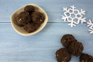 mavi ahşap masa yüzeyinde kağıt kar taneleri ve kase çikolatalı kurabiye