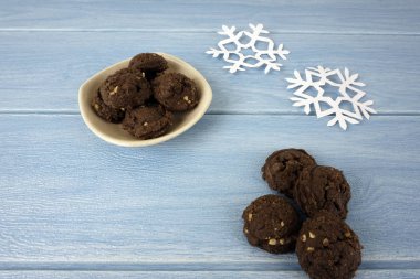 mavi ahşap masa yüzeyinde kağıt kar taneleri ve kase çikolatalı kurabiye