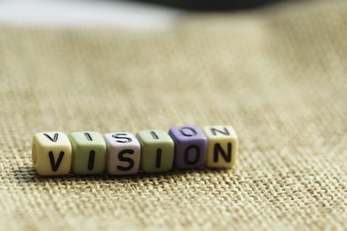 burlap kumaş tekstil yüzeyinde harflerle renkli küçük boncuklar, vizyon kavramı 