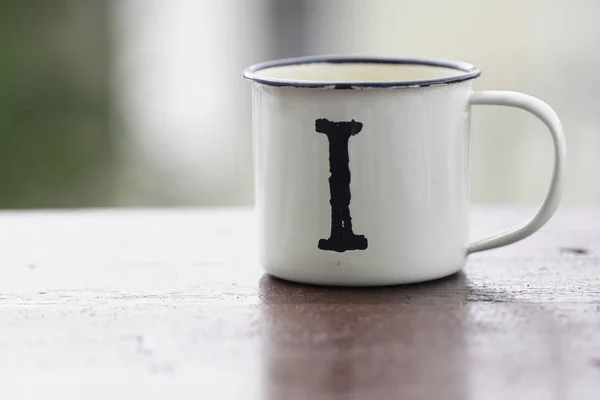 metallic travel white cup with letter i on wooden table