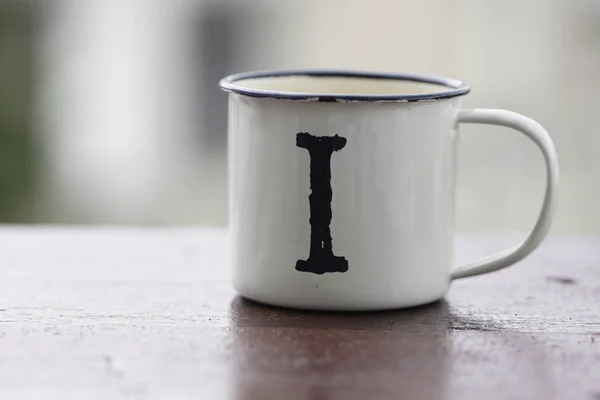 metallic travel white cup with letter i on wooden table