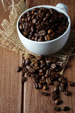 beyaz kahve fincanı ve kahverengi kavrulmuş kahve çekirdekleri burlap peçete ile masada 
