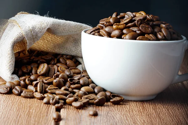 beyaz kahve fincanı ve kahverengi kavrulmuş fasulye çanta ile ahşap masa yüzeyinde 