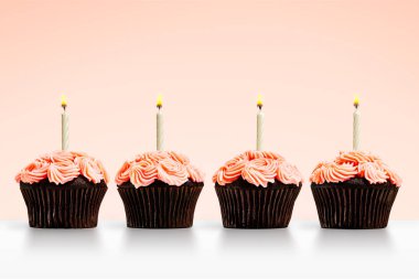 Pembe arka planda mumları olan bir sıra kek.