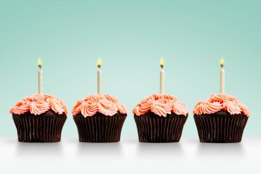 Yeşil arka planda mumları olan bir sıra kek.