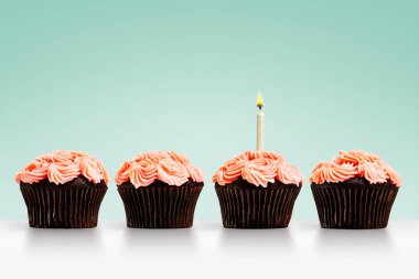 Yeşil arka planda tek bir mum olan bir sıra kek.