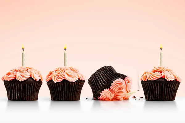 Σπασμένο κεκάκι στη σειρά από cupcakes με κεριά στο ροζ πίσω μέρος Φωτογραφία Αρχείου