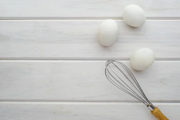 Felülnézet tojás habverővel és három tojást egy fehér fából készült asztal — Stock Fotó