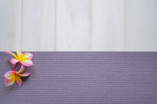 Plumeria flowers and purple yoga mat on a white wood floor