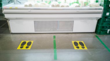 Bir alışveriş merkezinin sarı işaretli şeritleri, kuyruktaki müşterilere Corona virüsünden korunmak için doğru mesafeyi gösteriyor.