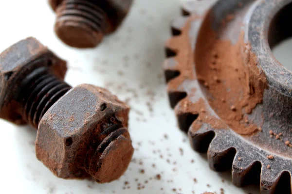 Rusty bolts, nuts and gear wheel made of chocolate on white background