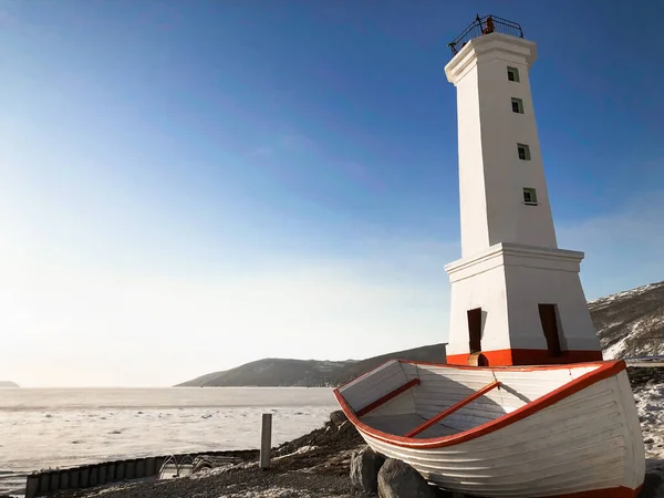 Magadan, Rusya 'nın deniz kıyısındaki eski deniz feneri ve ahşap teknenin resmi.