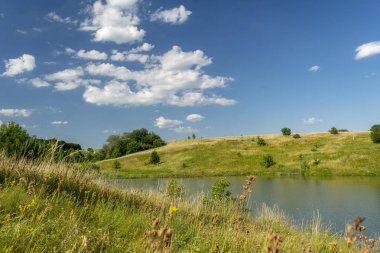 Nehrin, yeşil ağaçların, tepelerin ve mavi bulutlu gökyüzünün güzel manzarası. Yaz manzarası.