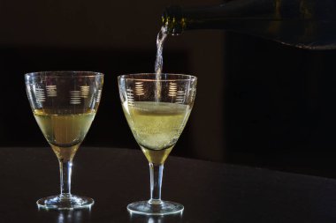 Şampanya, siyah arka plandaki bir şişeden bardağa dökülüyor..