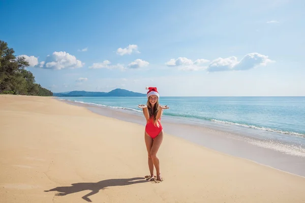 Молодая женщина в красном купальнике и шляпе Санта Клауса отправляет воздушный поцелуй — стоковое фото