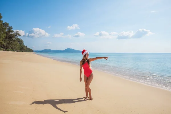 Jonge vrouw in rode zwembroek en kerstman hoed op het strand — Stockfoto