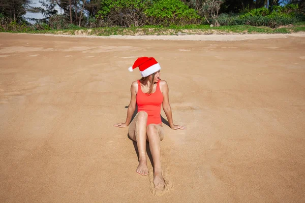 Молодая женщина в красном купальнике и шляпе Санта Клауса смотрит в камеру — стоковое фото