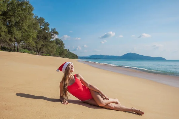 Молодая женщина в красном купальнике и шляпе Санта Клауса, лежащая на тропическом пляже — стоковое фото