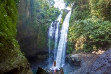 Aling-Aling şelale önünde kayaya oturan genç kadın