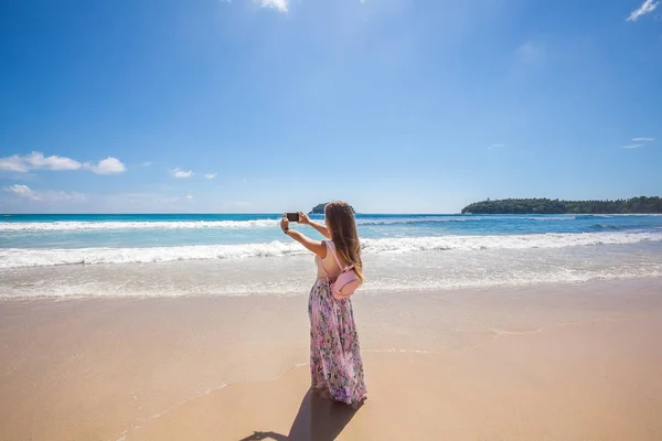 Dziewczyna w kwiatowy różowy spódnica maxi, biorąc obraz na brzegu morza — Zdjęcie stockowe